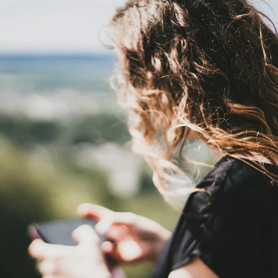 Woman with hair flowing in the wind texting on her phone