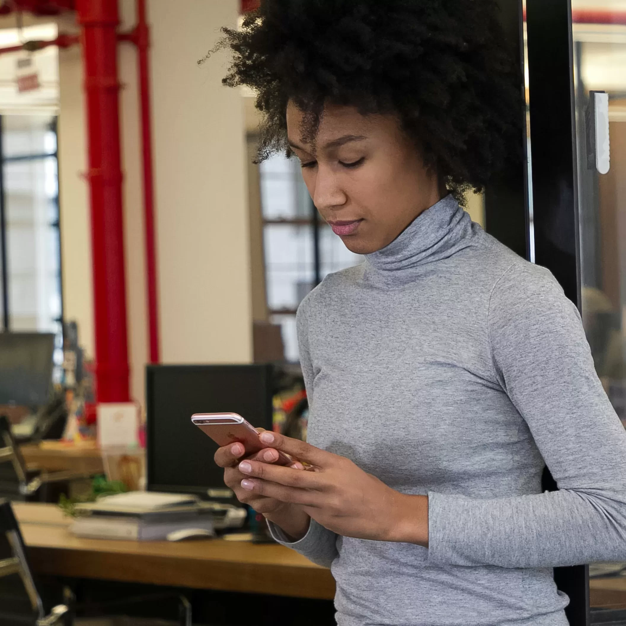 Privacy-Policy Woman looking at her phone in her private office with her back to the rest of the office