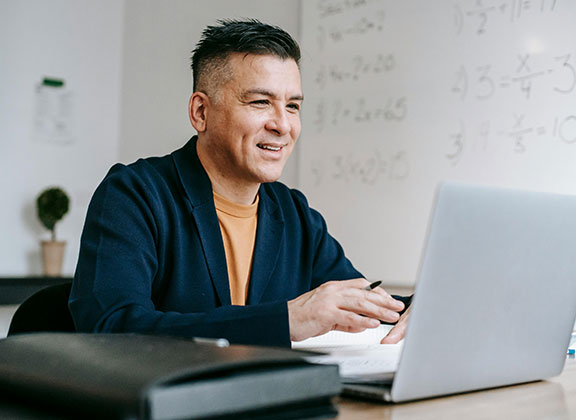 business man smiling while typing on his silver laptop