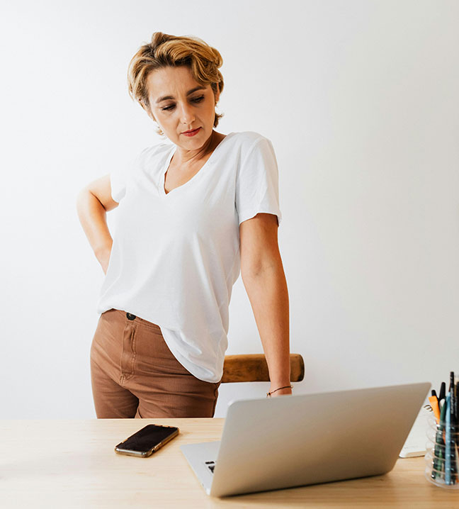 woman with her hand on her hip standing at a table and looking down at a laptop