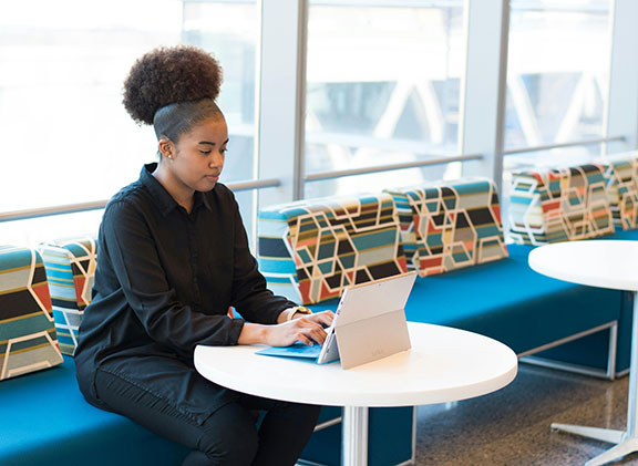 woman sitting on blue bench typing on a tablet
