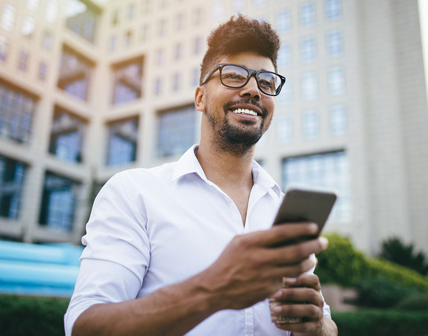man in a city looking up from his phone and smiling