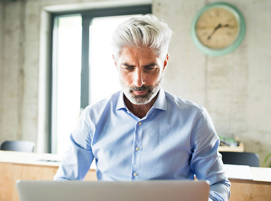 man with gray hair and button shirt looking at laptop