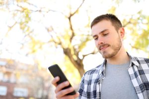 Man in plaid shirt, outside in the sun, reading a text message from a known Sender ID