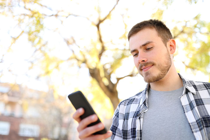 Man in plaid shirt, outside in the sun, reading a text message from a known Sender ID