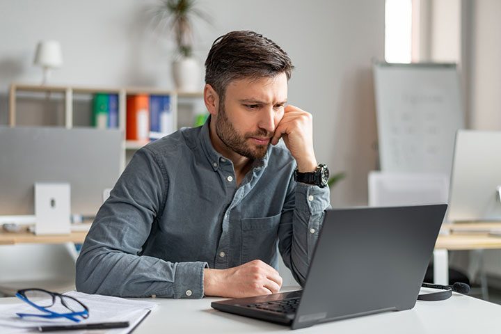 man sitting at desk looking intently at his laptop screen